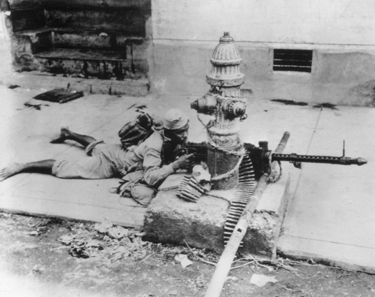 A Hukbalahap guerrilla fighter in Manila uses a fire hydrant as a make-shift tripod while firing at the Japanese.