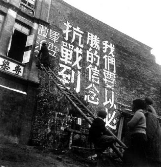 Individuals putting up propaganda on a building wall.